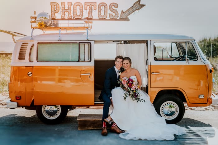 Bride and groom in a VW van photo booth. Bride is holding a cascading bouquet. Flowers by Eastern Floral.